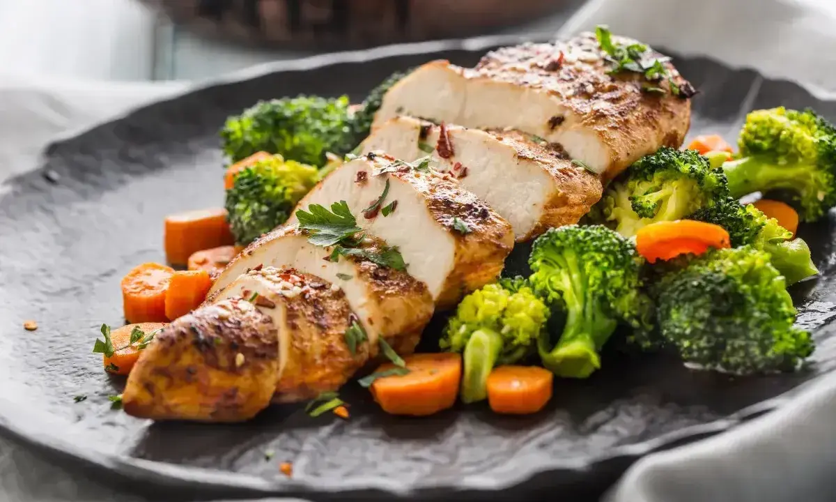 Soczysty filet drobiowy pokrojony w plastry, podany z chrupiącym brokułem i marchewką.