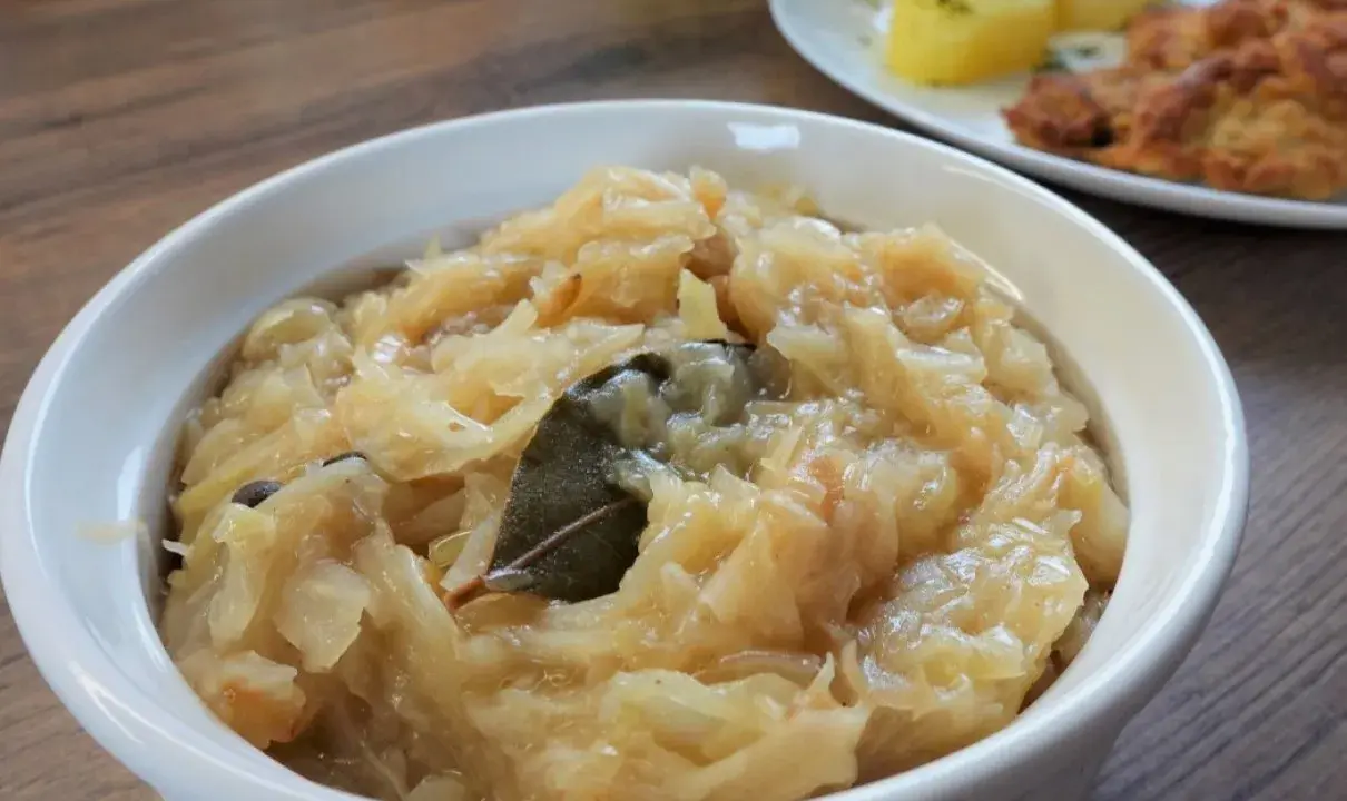 Pyszna, aromatyczna zasmażana kapusta kiszona z liściem laurowym i zielem angielskim, podana w białej miseczce.
