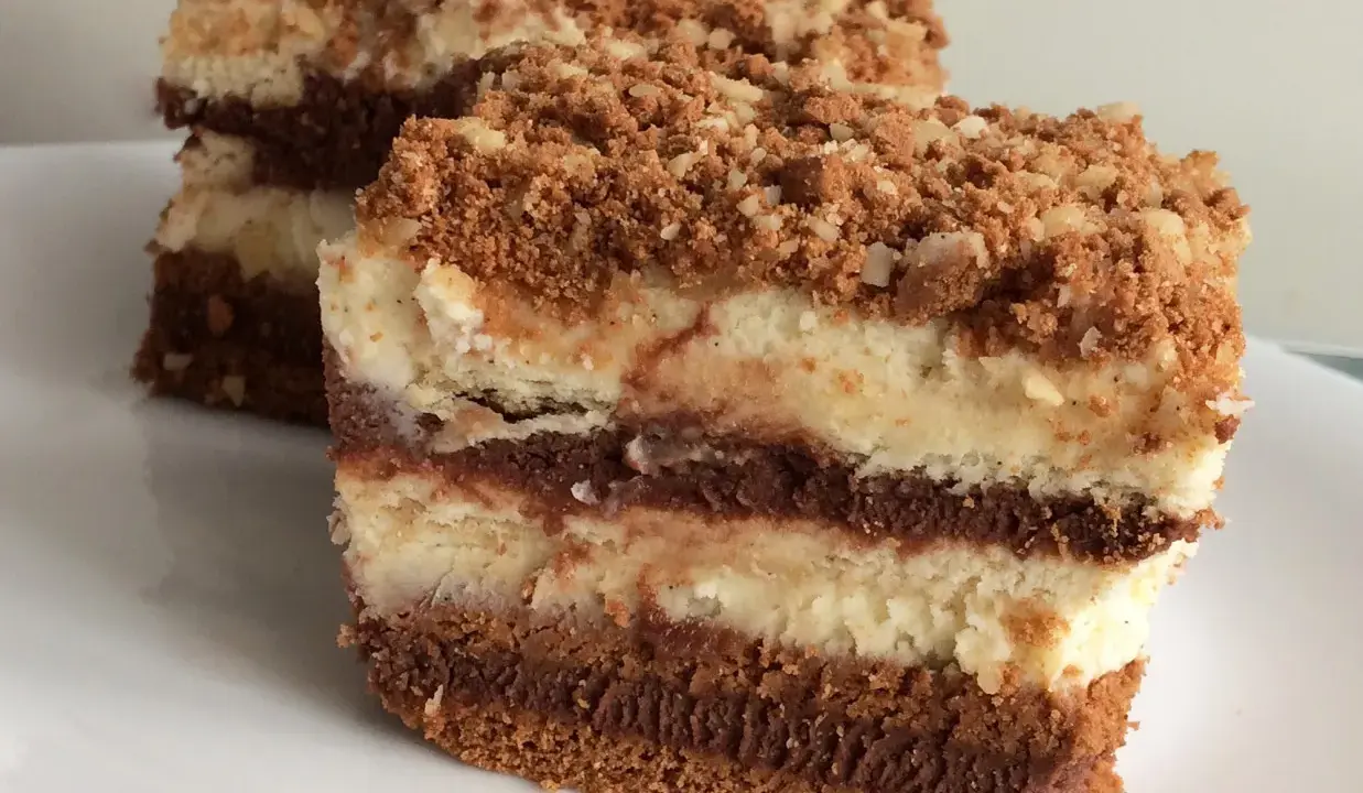 Warstwowe ciasto z serkiem mascarpone 250g, przełożone czekoladą i posypane kruszonką. Pyszny deser na talerzu.