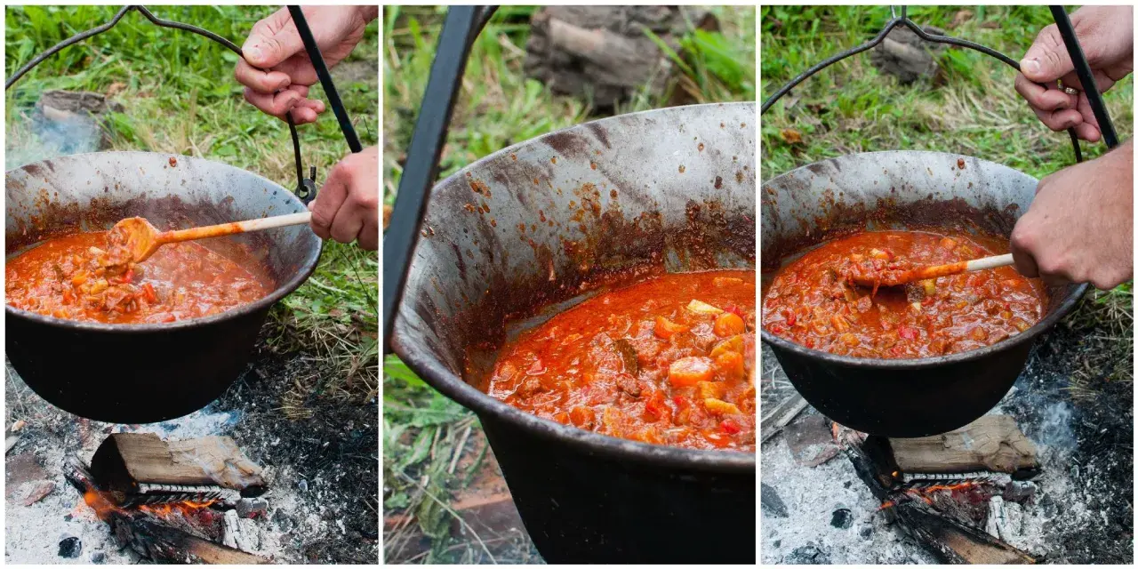 Gotowanie aromatycznego bogracza nad ogniskiem. Mieszanie drewnianą łyżką gęstej, czerwonej potrawy w kociołku.