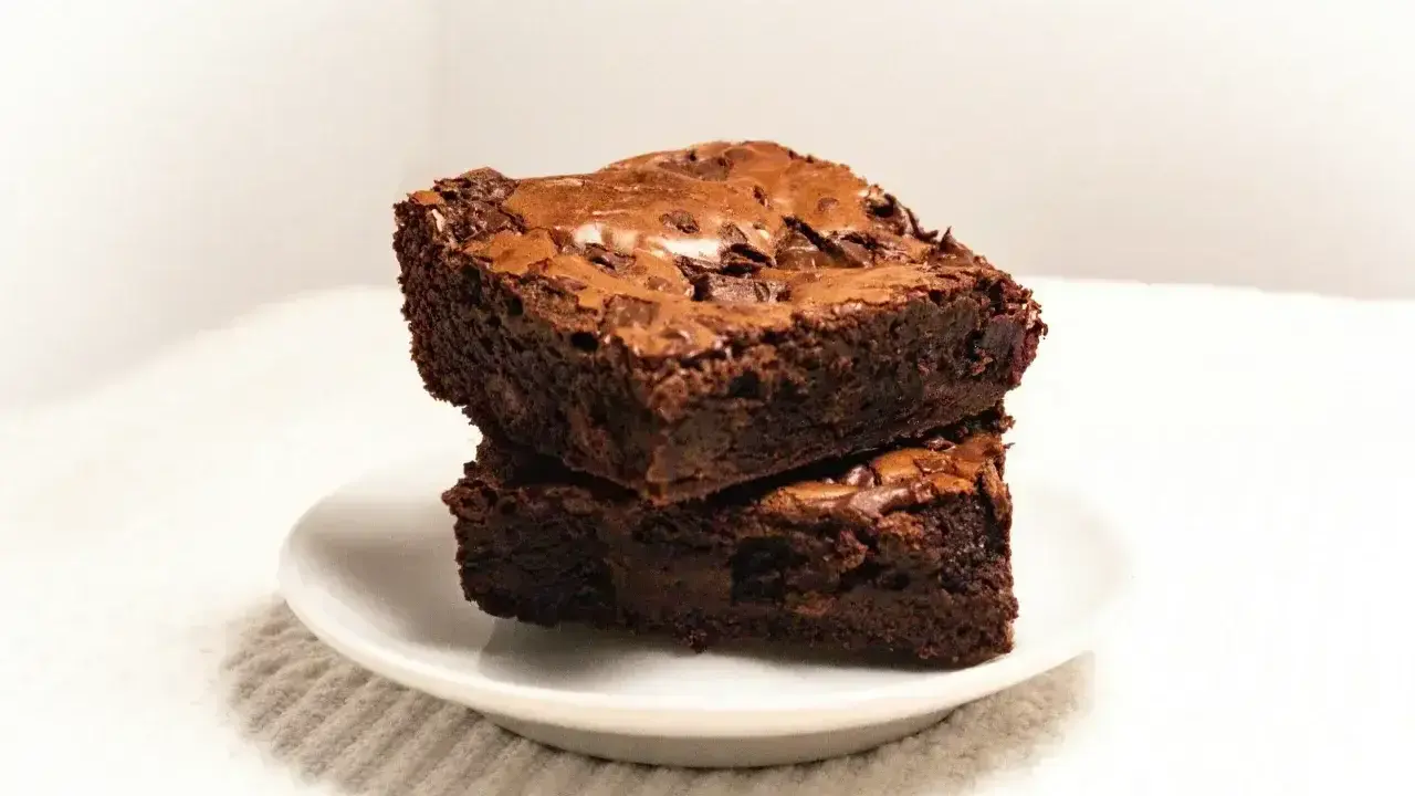 Dwa wilgotne ciasta brownie z płynną czekoladą, ułożone jedno na drugim na białym talerzyku.