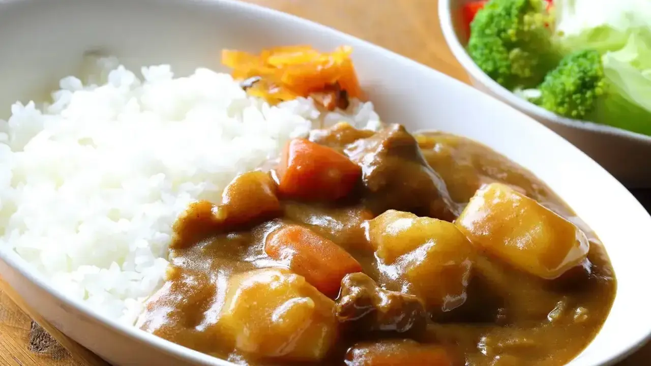 Pyszny ryż z curry, z kawałkami mięsa, ziemniaków i marchewki, podany z surówką.