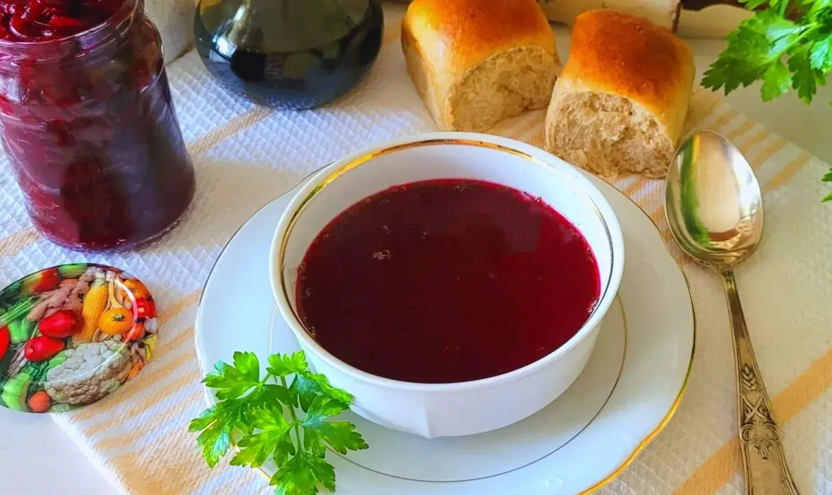 Aromaticzny barszcz czerwony z surowych buraków, podany z bułeczkami i słoikiem domowych przetworów.