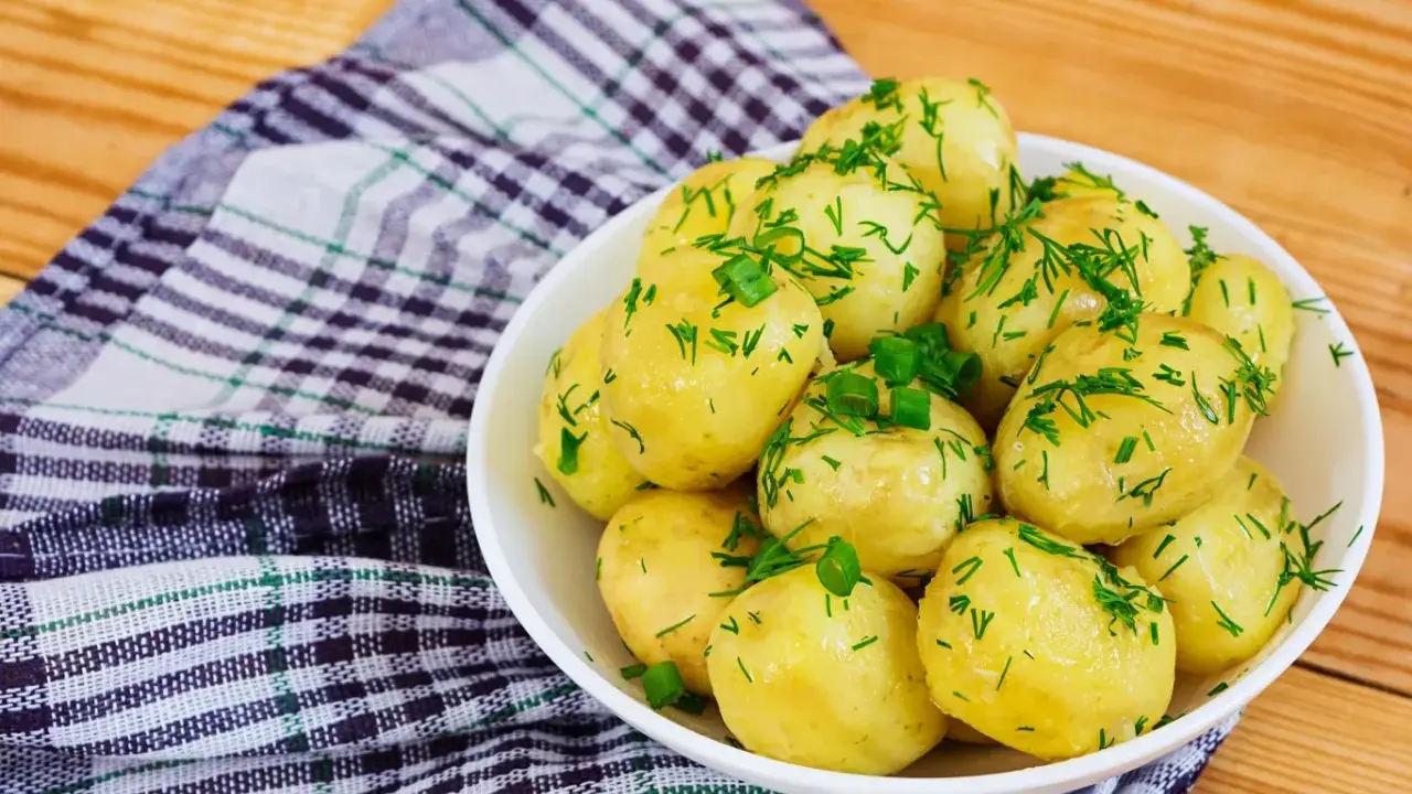 Młode ziemniaki w misce, posypane koperkiem i szczypiorkiem. Idealne na lato, a ile gotować młode ziemniaki? Krótko!