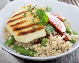 Kuskus z grillowanym serem halloumi, fasolką szparagową i figami, ozdobiony miętą.