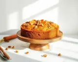 Pyszne ciasto bez glutenu, ozdobione pomarańczą i orzechami, prezentuje się apetycznie na drewnianej podstawce.
