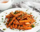 Karmelizowane marchewki z ziołami i parmezanem na białym talerzu.