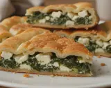 Pyszny borek ze szpinakiem i serem feta, posypany sezamem, prezentuje się apetycznie na białym talerzu.