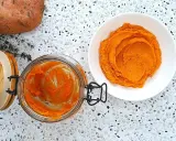 Pomarańczowe purée z batatów w słoiku i na talerzu, obok surowy batat i gałązka tymianku.