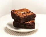 Dwa wilgotne ciasta brownie z płynną czekoladą, ułożone jedno na drugim na białym talerzyku.
