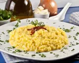 Aksamitne risotto alla milanese, ozdobione suszonymi papryczkami i natką pietruszki, prezentuje się apetycznie na białym talerzu.