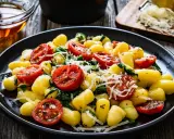 Gnocchi ze szpinakiem i pomidorkami koktajlowymi, posypane parmezanem, na czarnym talerzu.
