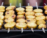 Ziemniaki z grilla, pokrojone w plastry i nabite na szpadki, pieką się na węglu. Apetyczny zapach unosi się w powietrzu.