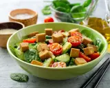 Pyszna sałatka z tofu, pomidorkami koktajlowymi, ogórkiem i szpinakiem, posypana sezamem. Idealna na lekki posiłek.
