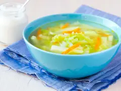 Aksamitna zupa z kalarepy z marchewką i ziemniakami, podana w błękitnej misce na niebieskiej serwetce. Obok słoiczek śmietany.