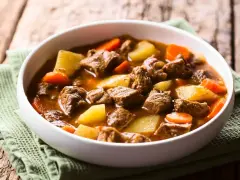 Gęsta zupa gulaszowa przepis babci z kawałkami wołowiny, ziemniaków i marchewki w białej misce na zielonej serwetce.