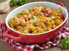 Zapiekanka makaronowa z kawałkami prosciutto cotto, zapieczona pod serem i udekorowana natką pietruszki.
