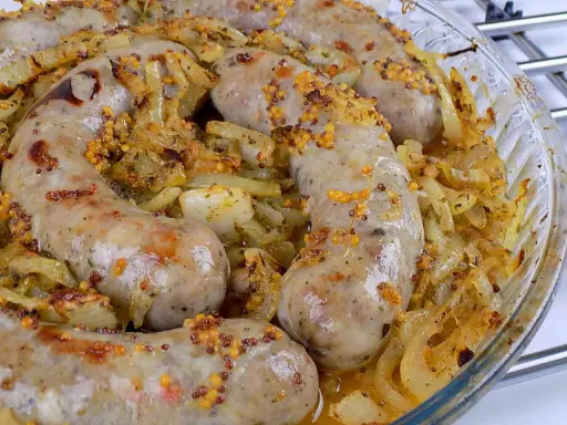 Biała kiełbasa surowa pieczona w piekarniku z cebulą i musztardą ziarnistą. Pyszne danie gotowe do podania.