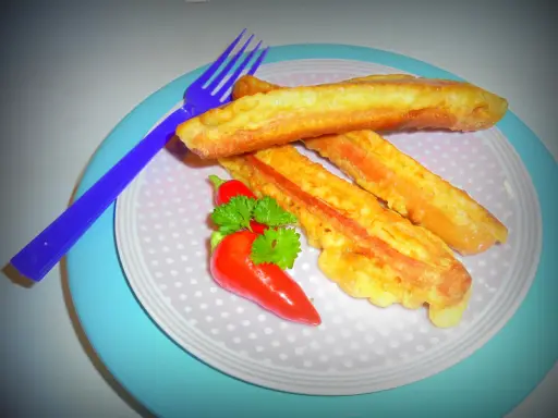 Parówki w cieście naleśnikowym, złociste i chrupiące, podane z papryczką chili i natką pietruszki.
