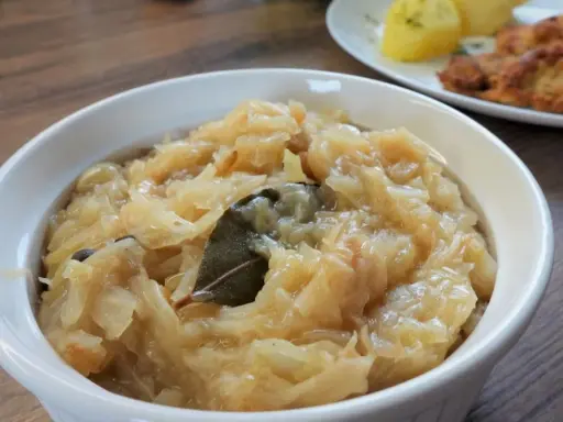 Pyszna, aromatyczna zasmażana kapusta kiszona z liściem laurowym i zielem angielskim, podana w białej miseczce.