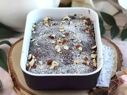 Pyszny brownie z mikrofali, posypany cukrem pudrem i orzechami, w białej ceramicznej formie.