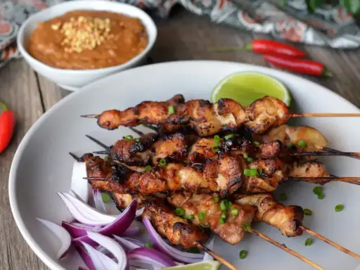 Pyszne satay z kurczaka na patyczkach, podane z sosem orzechowym, limonką i papryczkami chili.