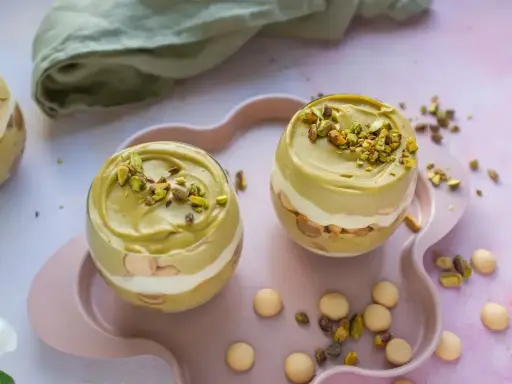 Dwa pucharki z kremem pistacjowym z mascarpone, udekorowane posiekanymi pistacjami.