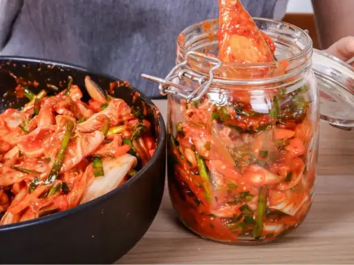Domowe kimchi w słoiku i misce, przygotowywane z kapusty i przypraw.