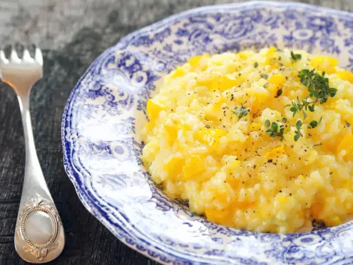 Pyszny, kremowy ryż do risotto z kawałkami dyni, posypany świeżym tymiankiem i pieprzem. Obok leży elegancki widelec.