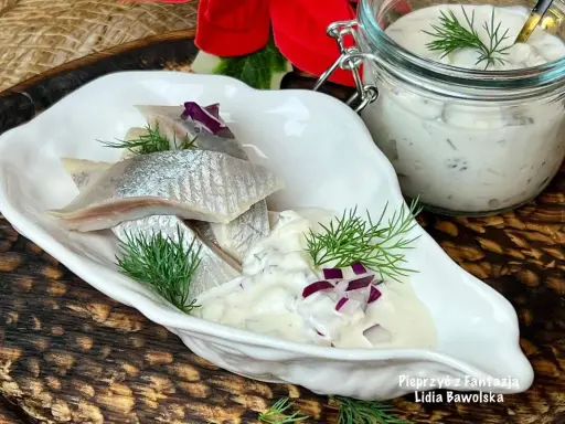 Matiasy w śmietanie z cebulą i ogórkiem, udekorowane koperkiem, prezentują się apetycznie.