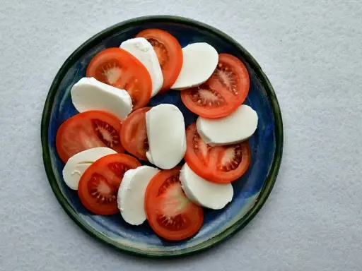 Plasterka pomidorów i mozzarelli ułożone naprzemiennie na niebieskim talerzu.