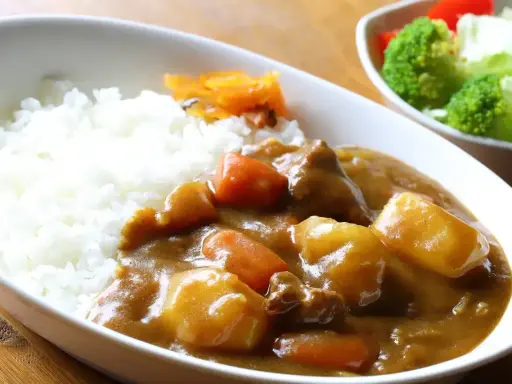 Pyszny ryż z curry, z kawałkami mięsa, ziemniaków i marchewki, podany z surówką.