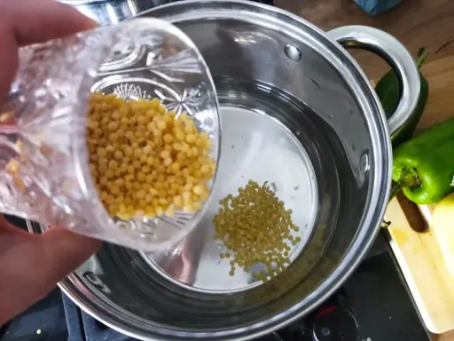 Wsypuję kaszę kuskus perłową do gotującej się wody w garnku.