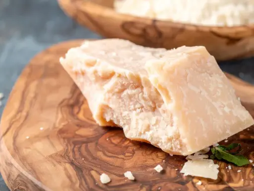 Kawałek twardego sera Grana Padano na drewnianej desce. Czy Grana Padano to parmezan? To pytanie często zadawane przez miłośników włoskich serów.