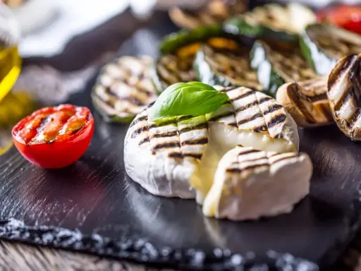 Grillowany camembert z pomidorkiem, cukinią i pieczarkami na czarnej desce.