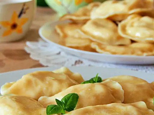 Słowackie pierogi z bryndzą na talerzu, ozdobione listkami bazylii.
