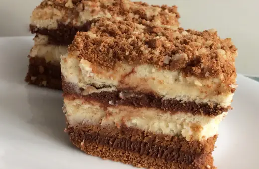 Warstwowe ciasto z serkiem mascarpone 250g, przełożone czekoladą i posypane kruszonką. Pyszny deser na talerzu.