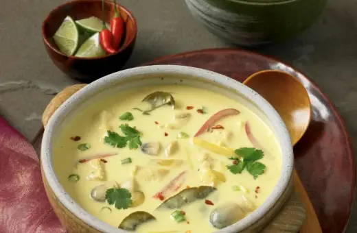 Aromatyczna zupa tajska z kurczakiem i mlekiem kokosowym, ozdobiona kolendrą i papryczkami chili.