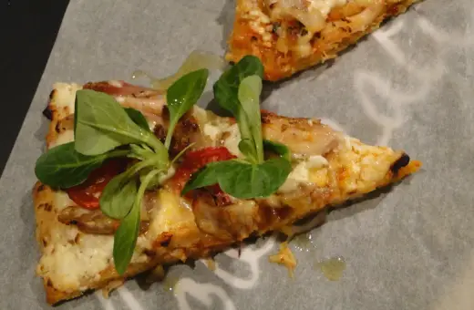 Dwie porcje pizzy z twarogu, z pomidorkami i świeżymi ziołami, na papierze do pieczenia.
