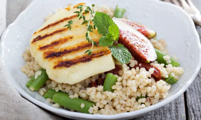 Kuskus z grillowanym serem halloumi, fasolką szparagową i figami, ozdobiony miętą.