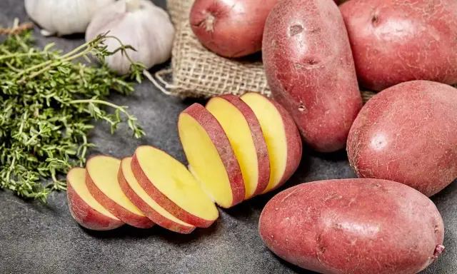 Czerwone ziemniaki, jeden pokrojony w plastry, obok czosnku i ziół.
