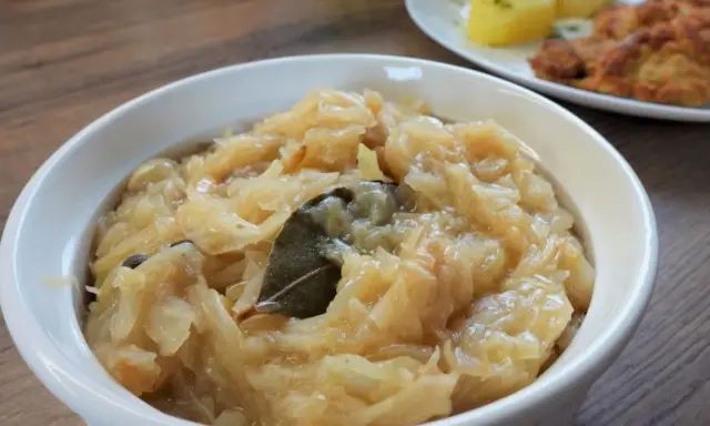 Pyszna, aromatyczna zasmażana kapusta kiszona z liściem laurowym i zielem angielskim, podana w białej miseczce.