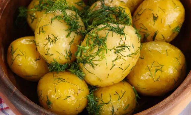 Ziemniaki gotowane w drewnianej misce, posypane świeżym koperkiem. Aromatyczne i apetyczne danie.