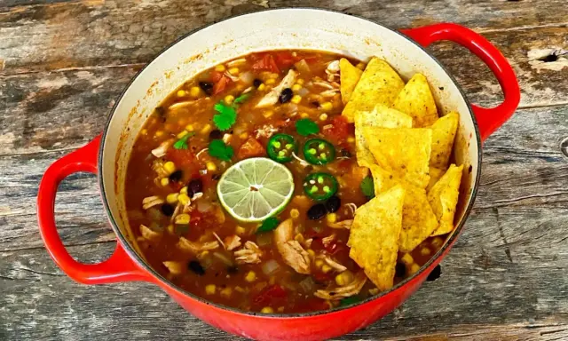 Prawdziwa zupa meksykańska w czerwonym garnku, pełna kurczaka, fasoli, kukurydzy, z limonką i jalapeño. Chrupiące nachos na wierzchu.