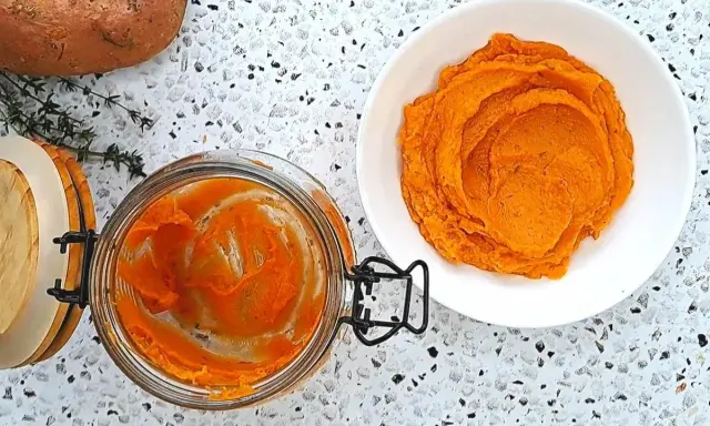 Pomarańczowe purée z batatów w słoiku i na talerzu, obok surowy batat i gałązka tymianku.