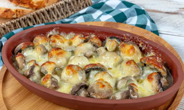Pieczarki zapiekane z serem w glinianym naczyniu, obok koszyk z pieczywem.