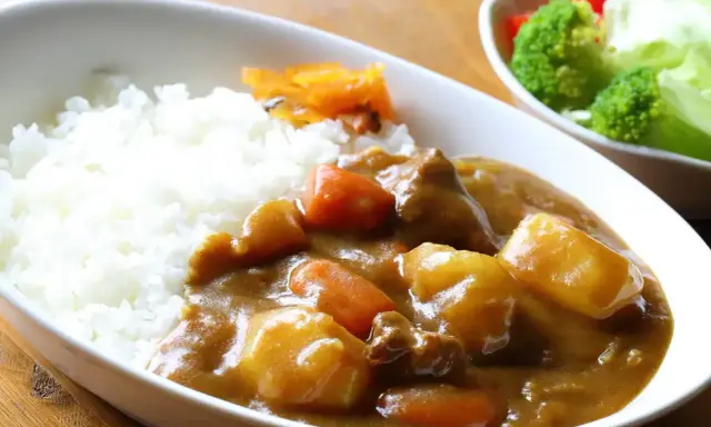 Pyszny ryż z curry, z kawałkami mięsa, ziemniaków i marchewki, podany z surówką.