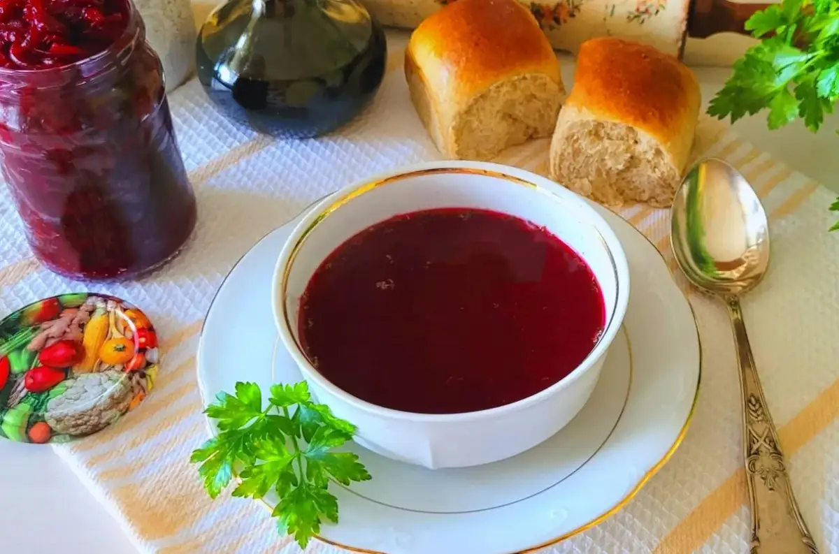 Aromaticzny barszcz czerwony z surowych buraków, podany z bułeczkami i słoikiem domowych przetworów.