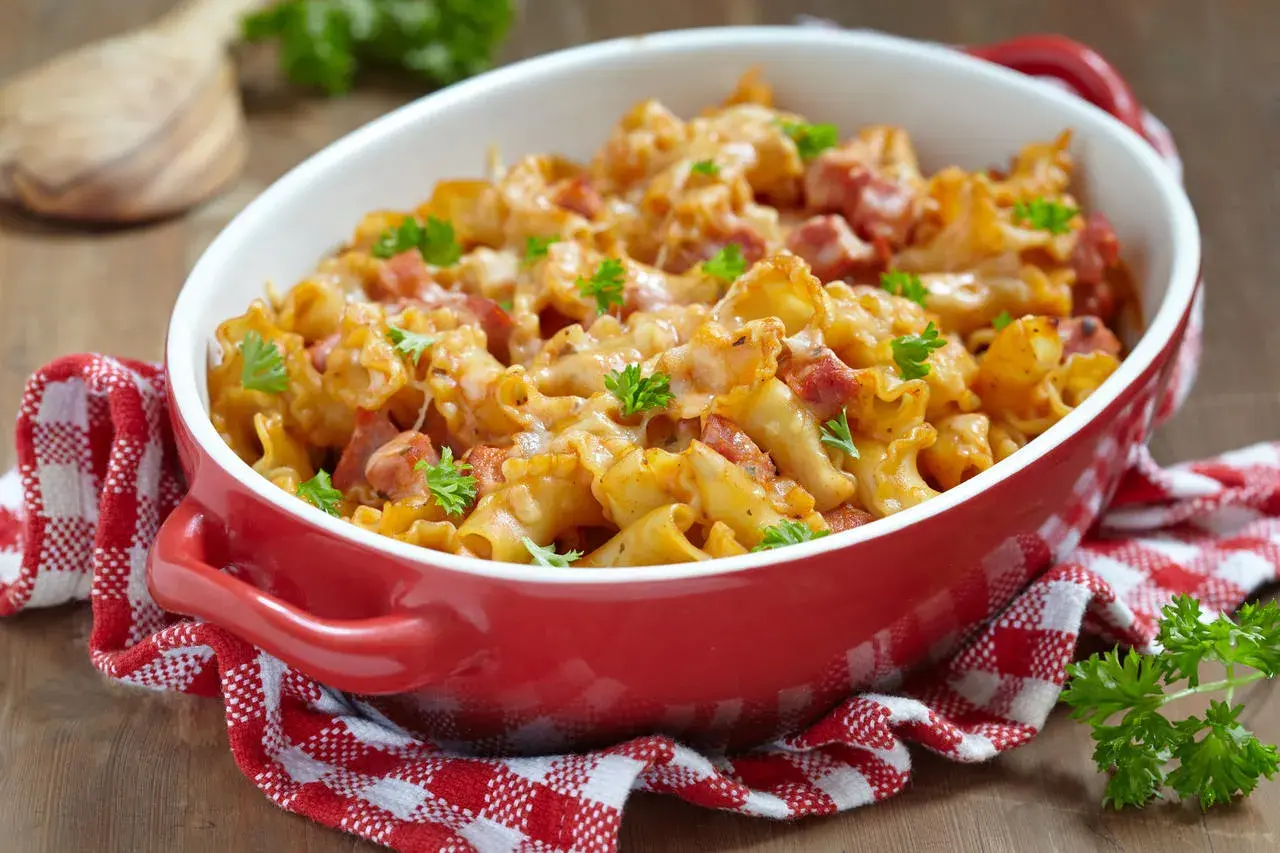Zapiekanka makaronowa z kawałkami prosciutto cotto, zapieczona pod serem i udekorowana natką pietruszki.