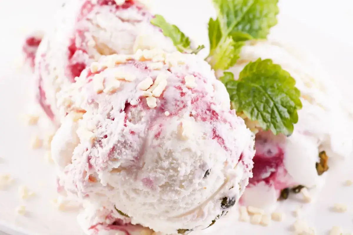 Pyszne lody z mascarpone, z malinowymi smugami i chrupiącymi kawałkami białej czekolady, ozdobione listkiem mięty.